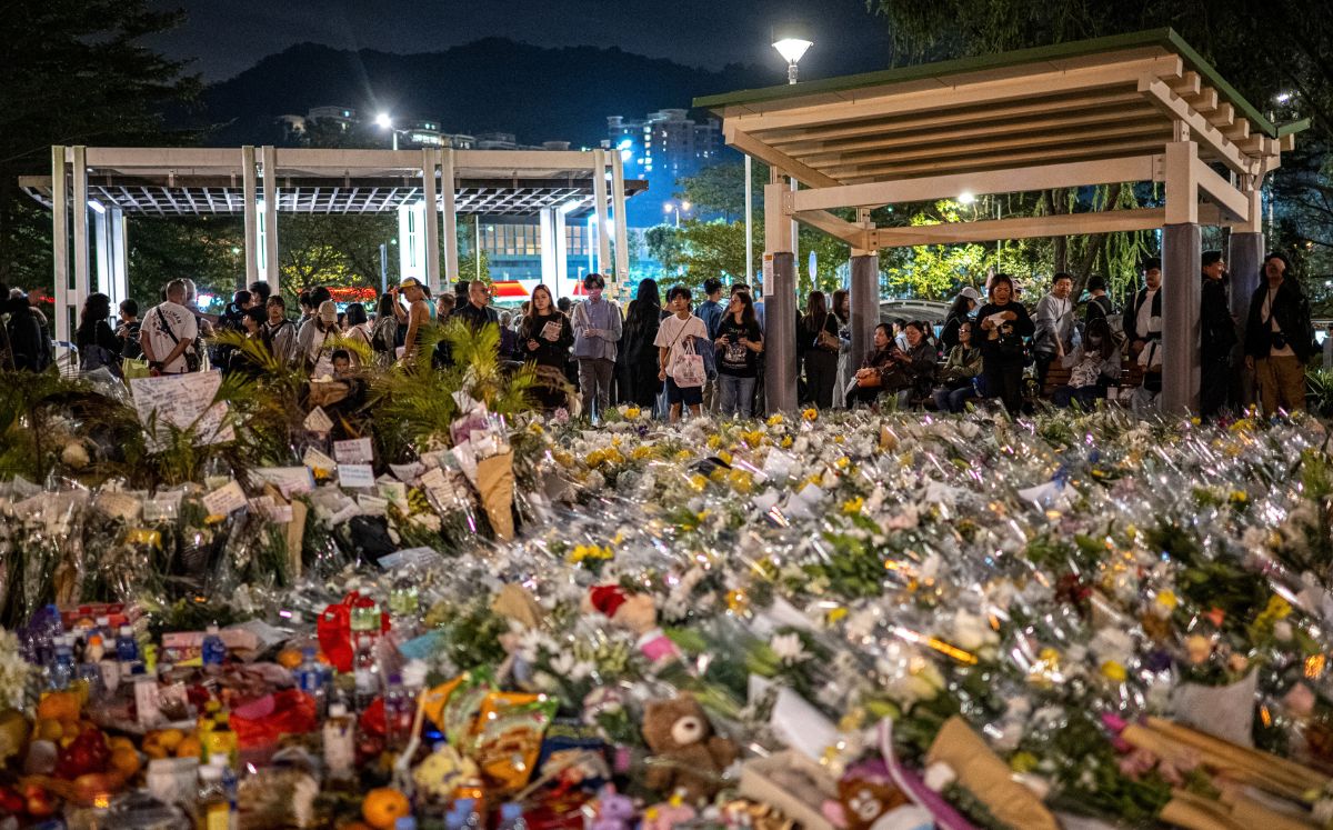 Personas depositan flores afuera de los bloques de apartamentos de Wang Fuk Court después del mortal incendio. (AFP)